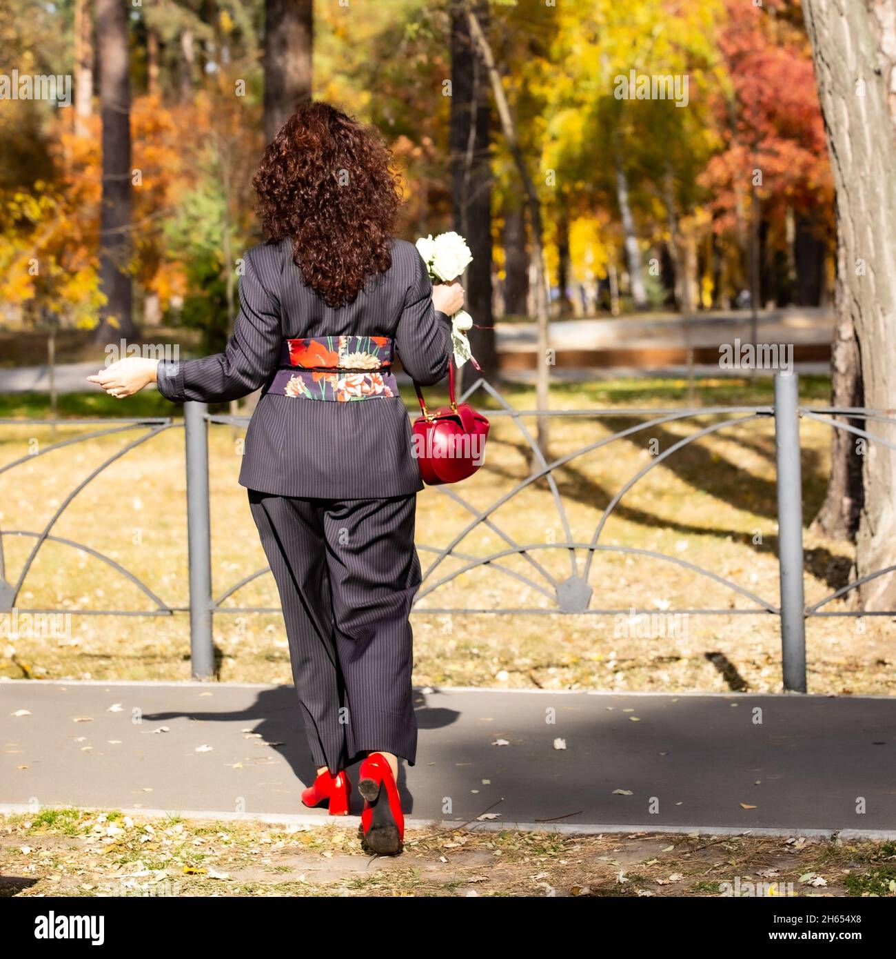 A young (30-40) Ukrainian woman in designer made suit with a broad waist belt on a wedding photo session in one of Kiev parks on a sunny October day. Stock Photo