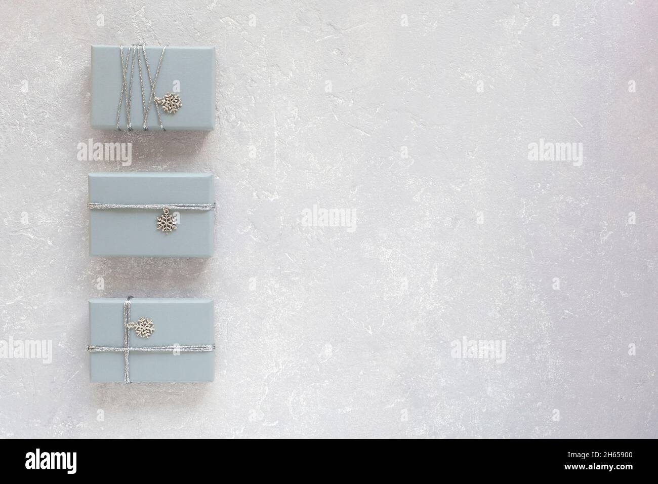 three grey gift boxes decorated with silver ribbon and snowflake pendant, on grey background, top view, copy space Stock Photo