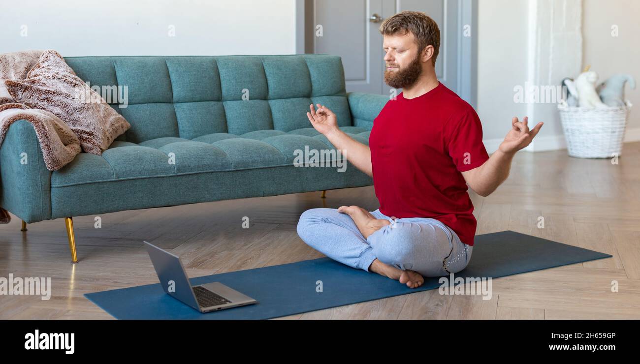 Mental health concept - middle-aged man taking an online yoga class. He is meditating in front of a laptop monitor. Format photo 2x1. Stock Photo
