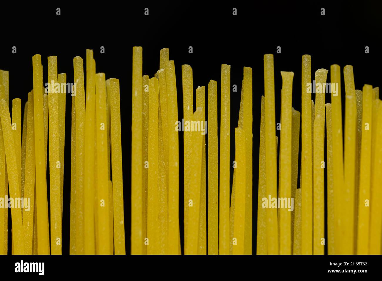 Some raw spaghetti noodles in vertical position in front of a deep black background. Stock Photo