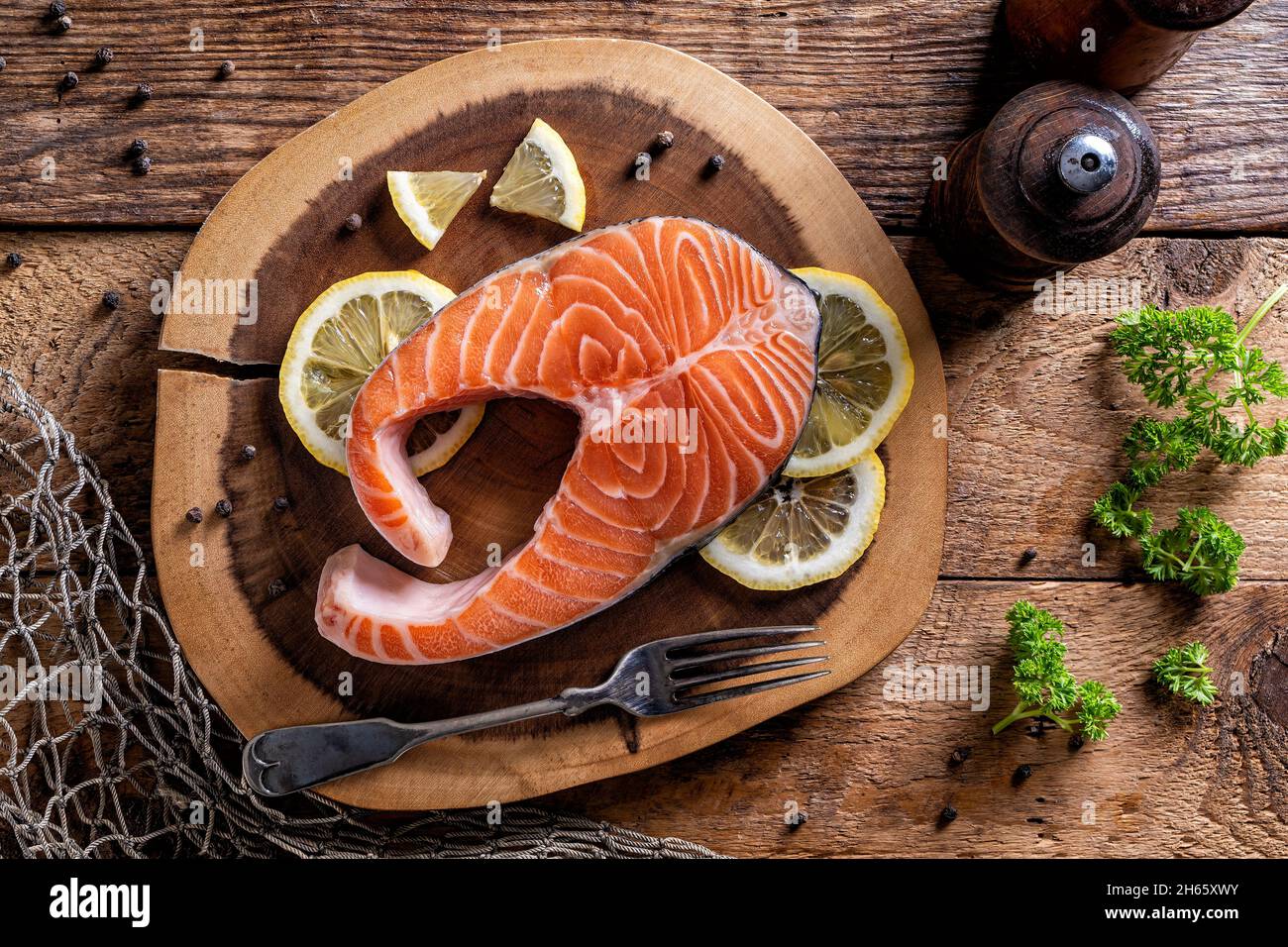 An Atlantic Salmon steak on a rustic wood table top with lemon, peppercorn and parsley. Stock Photo