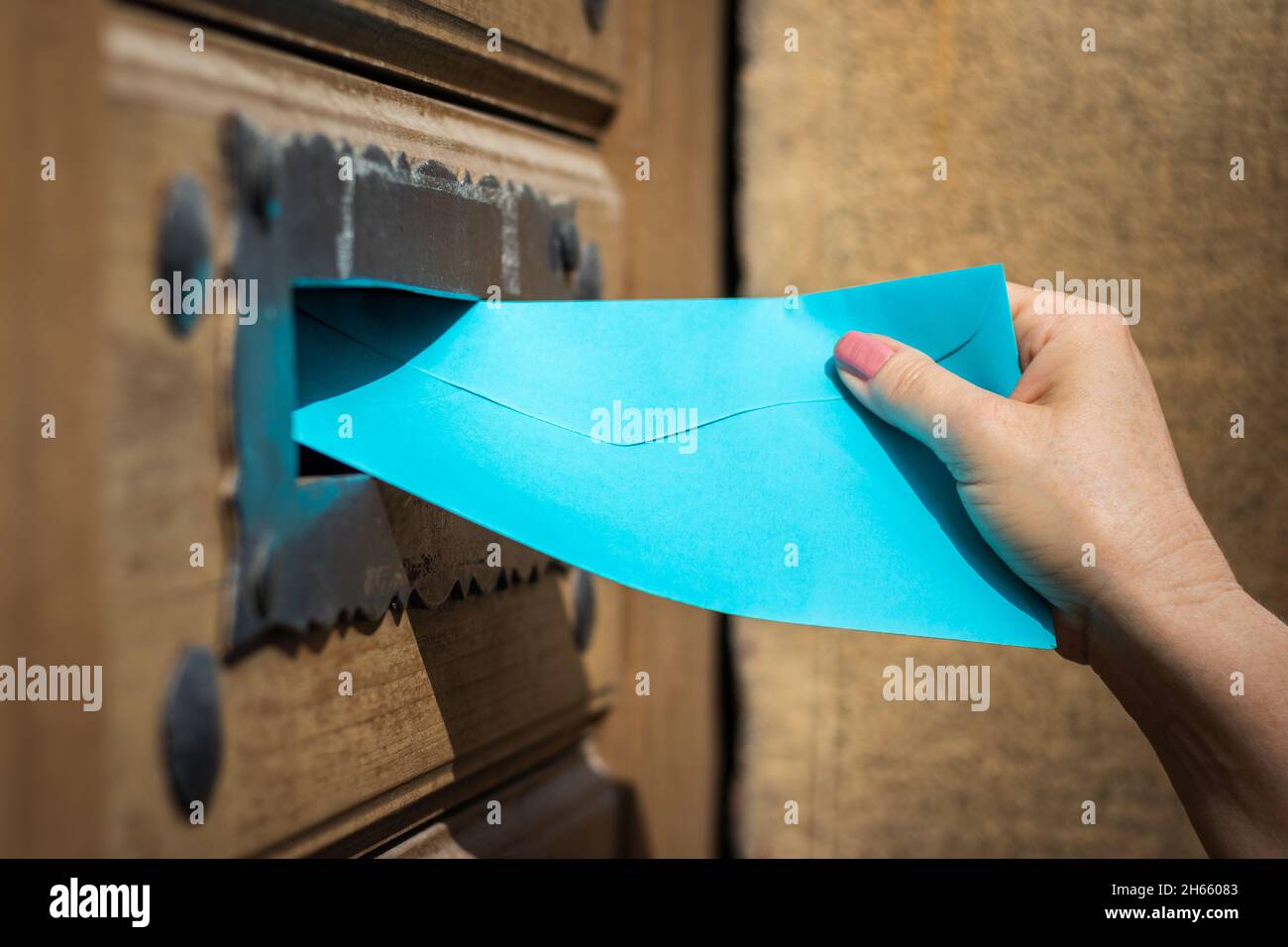 Woman inserting blue envelope into mail slot. Delivering letter by mail ...