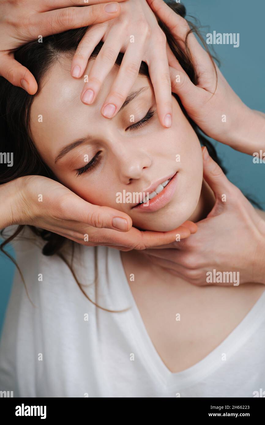 Joyous woman having pleasurable face massage with several beauticians hands touching her face. Stock Photo