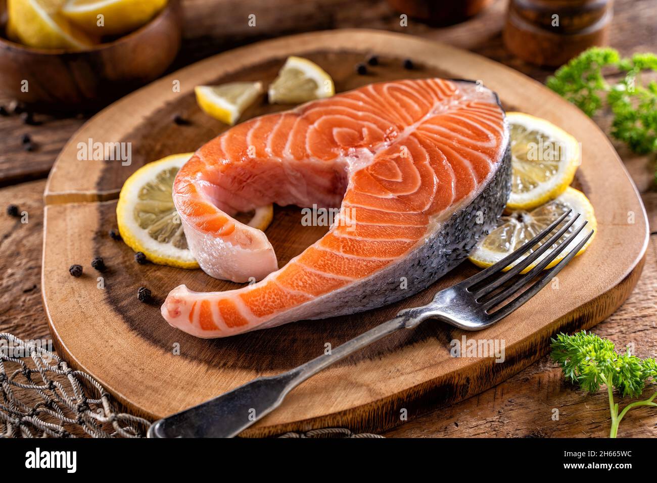 A fresh salmon steak on a rustic wood table top with lemon, peppercorn and parsley. Stock Photo