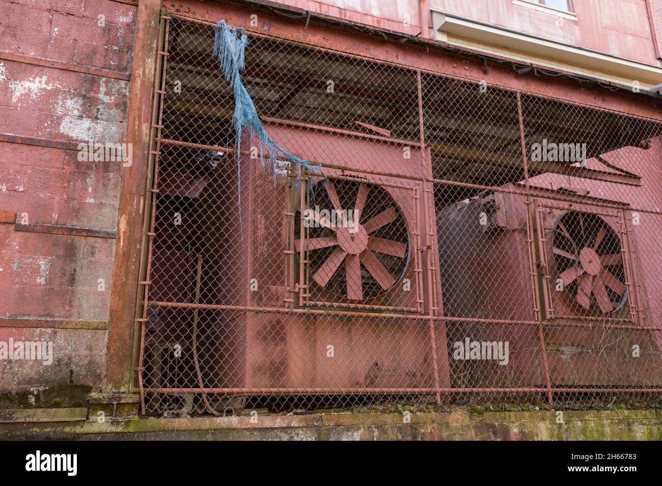 Old Industrial Building with large fans and chain link fence Stock Photo