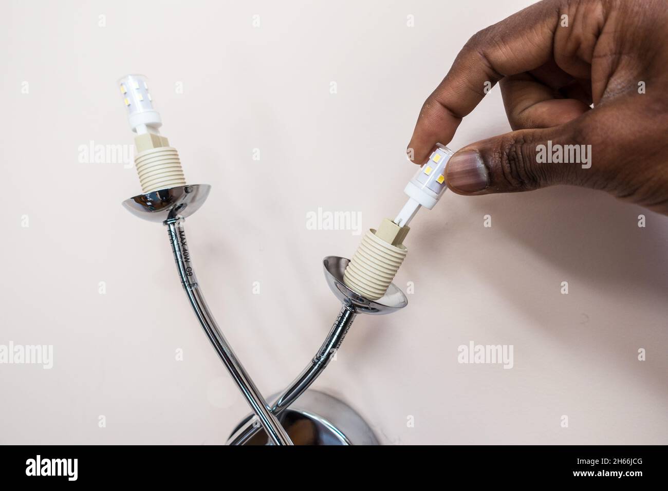 Adult male hand replacing a wall light bulb with LED energy saving bulb ...