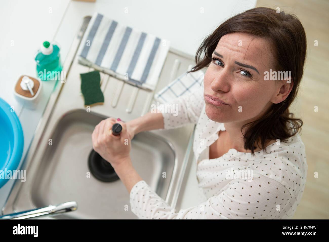 woman using plunger in blocked kitchen sink Stock Photo Alamy