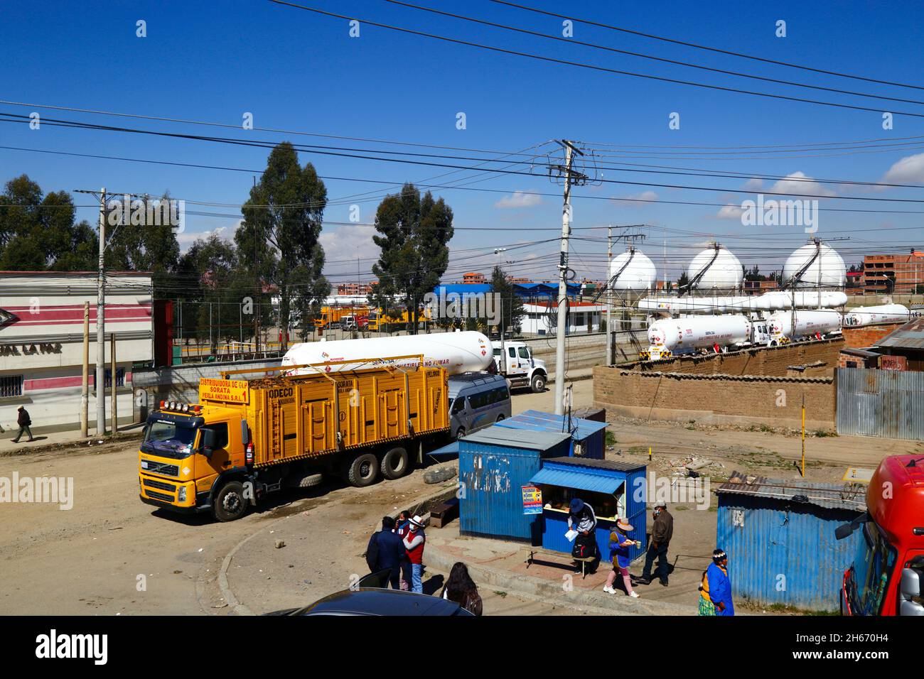 Senkata, El Alto, Bolivia. 13th November 2021. Liquid Natural Gas tank trucks and a domestic bottled gas delivery truck (yellow) outside the Senkata Fuel Plant on Av 6 de Marzo / Camino Oruro in El Alto. Yacimientos Petrolíferos Fiscales Bolivianos (YPFB, Bolivia's state owned oil and gas company) have a large refinery and storage plant here, which supplies La Paz, El Alto and the surrounding area with petrol / gasoline, diesel and liquid natural gas (in bottles for domestic use and also for vehicles and other industries). In the background are some of the spherical gas storage tanks. Stock Photo