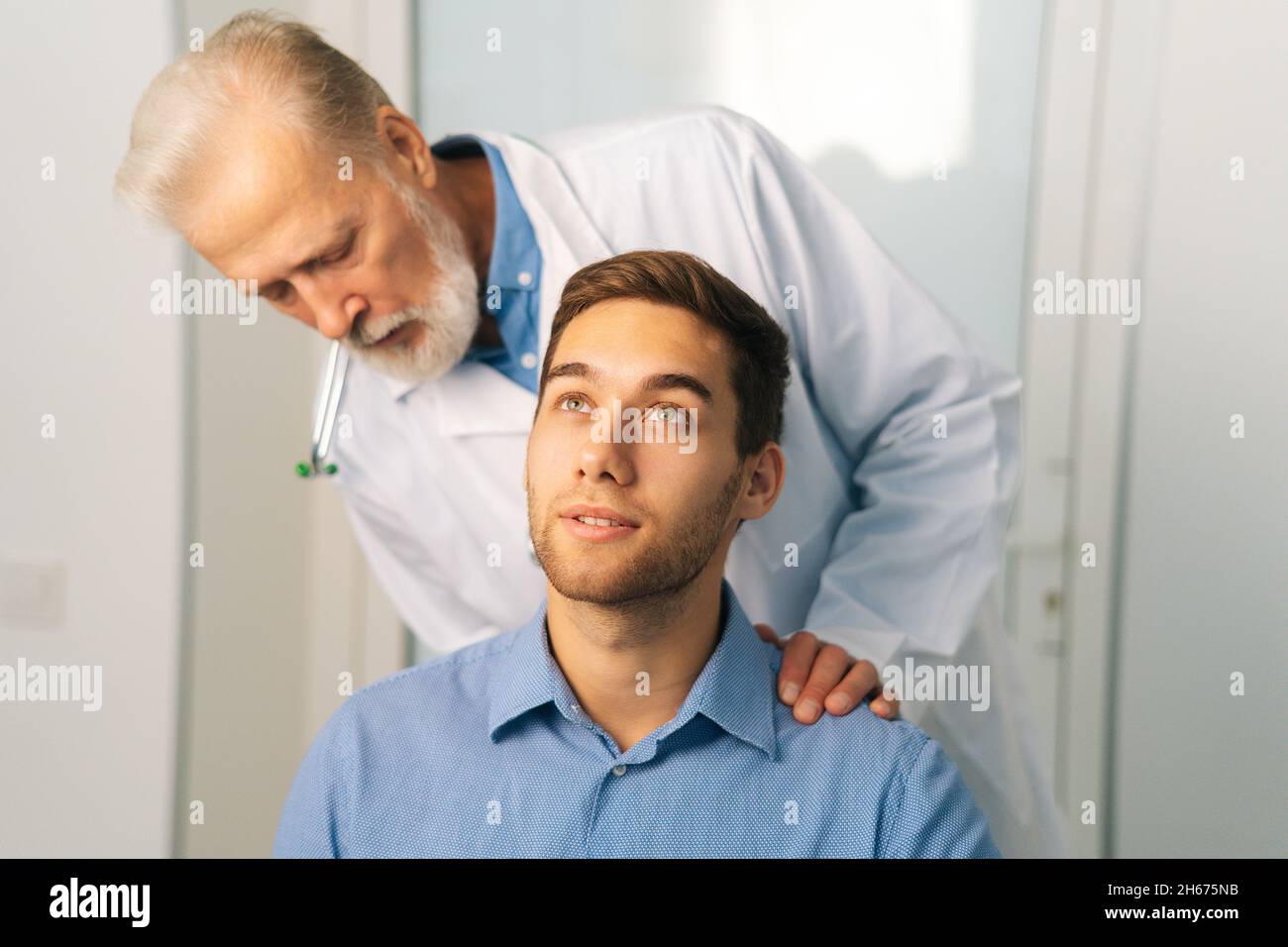 https://c8.alamy.com/comp/2H675NB/close-up-of-mature-adult-male-doctor-chiropractor-osteopath-talking-with-young-man-patient-sitting-in-chair-asks-about-problems-2H675NB.jpg