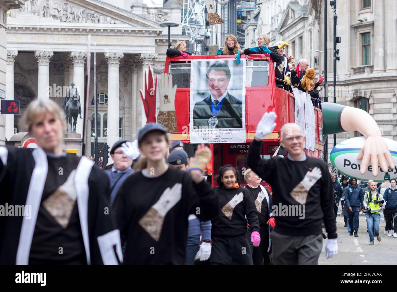 Members from The Worshipful Company of Glovers of London seen waving on a bus, with a picture of Lord Mayor Alderman Vincent Keaveny attached on its front, during the parade.The Lord Mayor's Show dates back to the early 13th century, when King John rashly allowed the City of London to appoint its own Mayor. Every year, the newly-elected Mayor tours the city in a golden carriage to swear loyalty to the Crown. This year, Alderman Vincent Keaveny was elected as the 693rd Lord Mayor of the City of London. The parade begins at Mansion House. Stock Photo