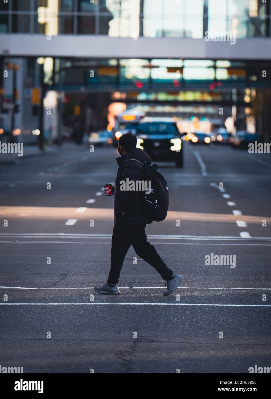 CALGARY, CANADA - Oct 16, 2021: A man holding a Tim Horton's cup crosses the street downtown Calgary, Alberta. Stock Photo