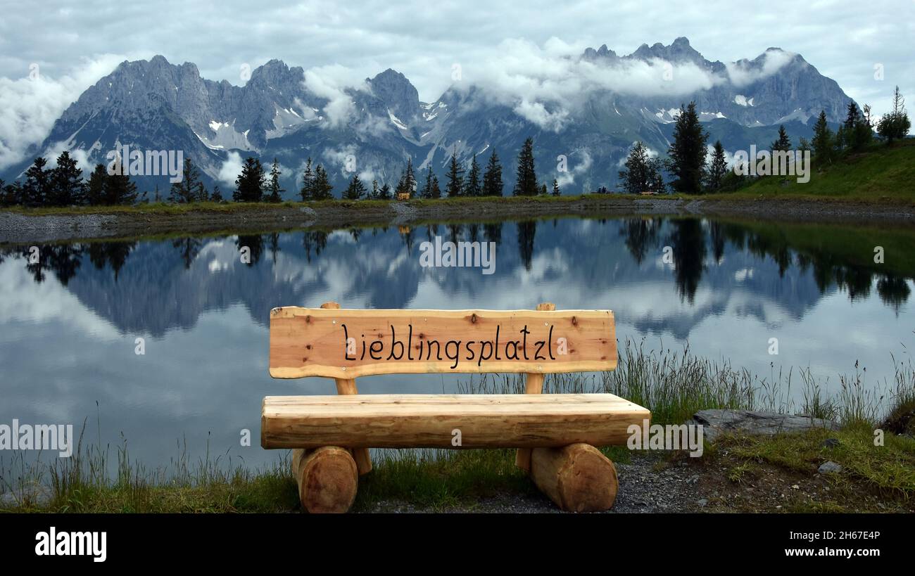 Reflection of “Wilder Kaiser“ mountains in Astberg Lake on a cloudy day behind a Bench. Going, Austria. Stock Photo