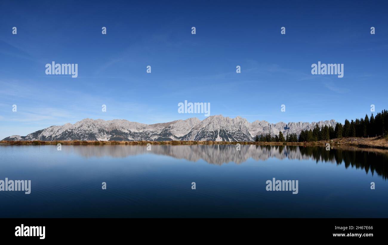 Reflection of “Wilder Kaiser“ mountains in a reservoir lake on a sunny day with blue sky. Scheffau, Austria. Stock Photo