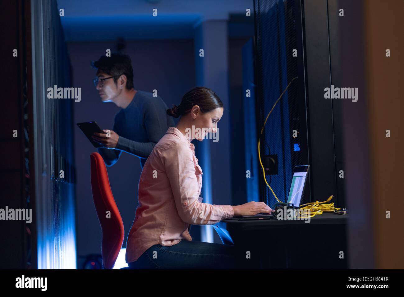 Caucasian female engineer using laptop and asian male engineer inspecting in computer server room Stock Photo