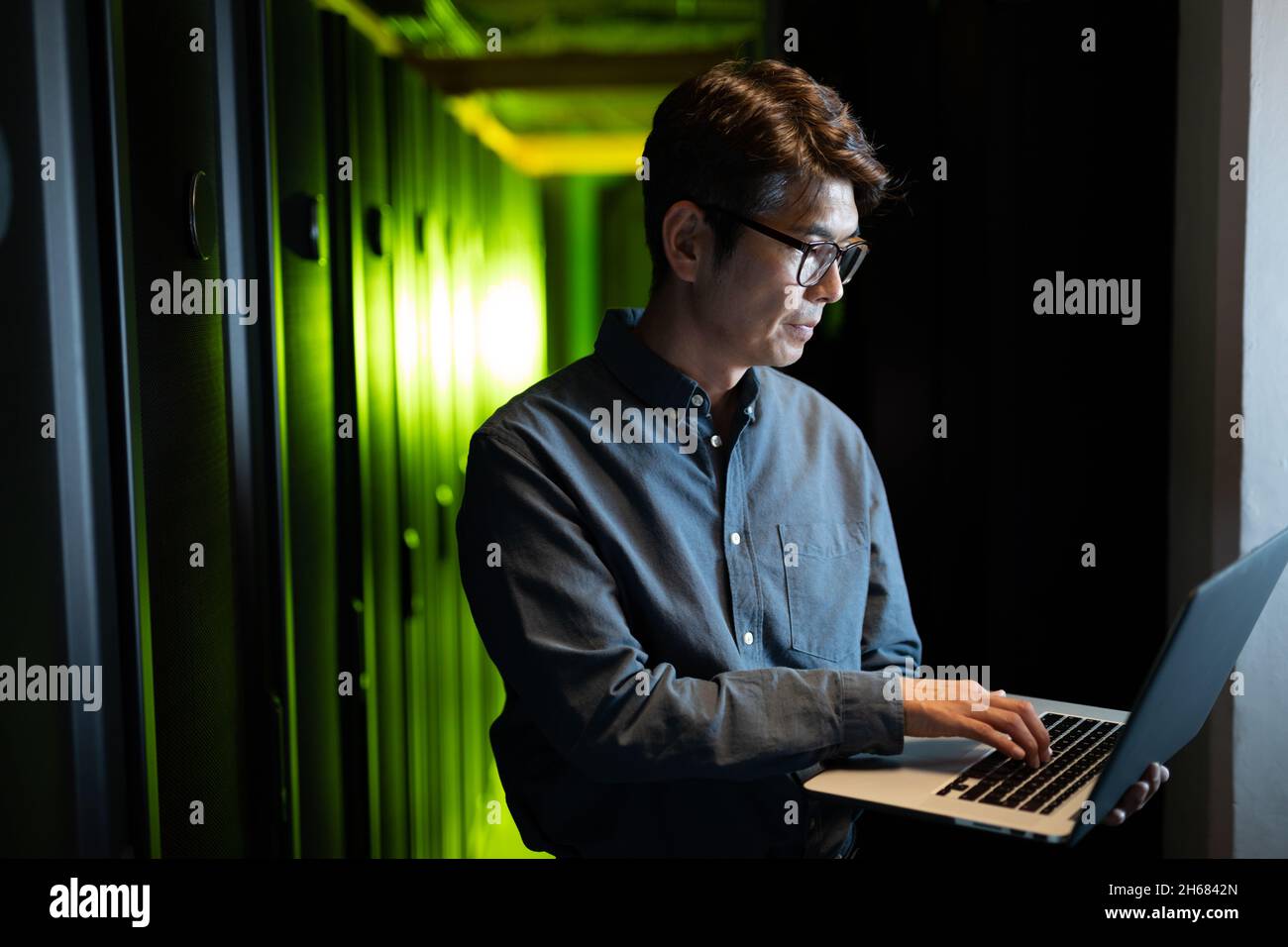 Asian male engineer using laptop in computer server room Stock Photo