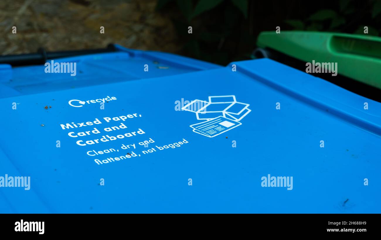 A blue paper recycling trash can in a garden with instructions written on the lid Stock Photo