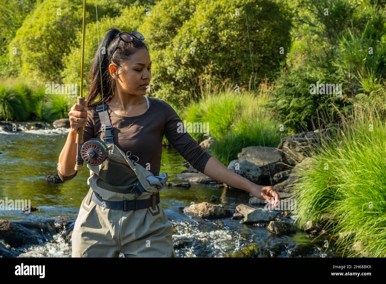 A young asian female standing fly fishing in a riffle on a river