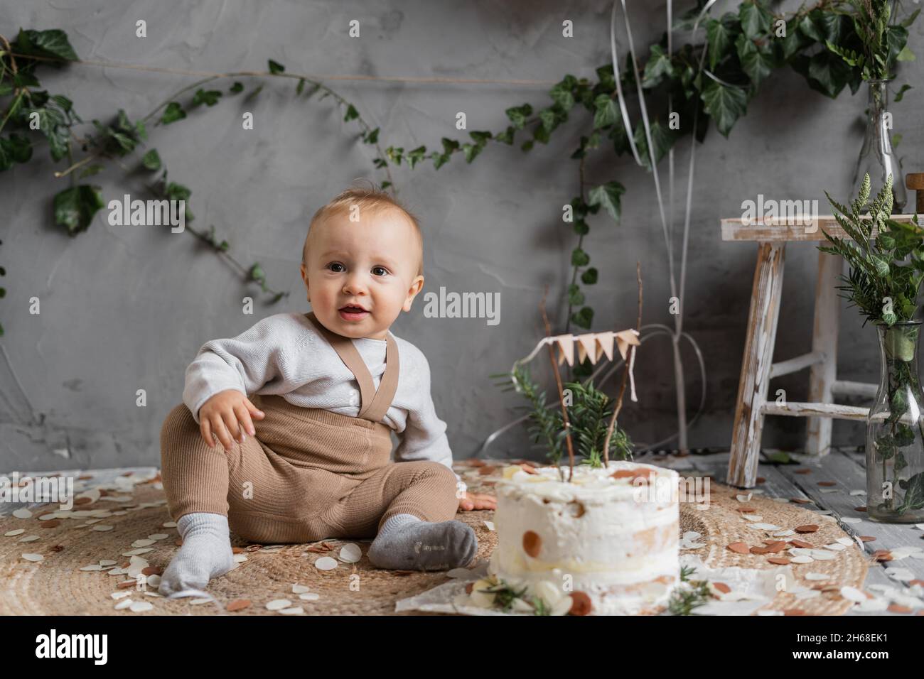 holiday baby's first birthday, boy with a delicious cake sitting on the floor, birthday in rustic style, natural photo zone, happy one year old. Stock Photo