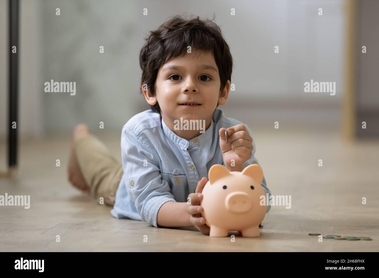 Indian preschool boy putting coin into pink piggy bank Stock Photo - Alamy