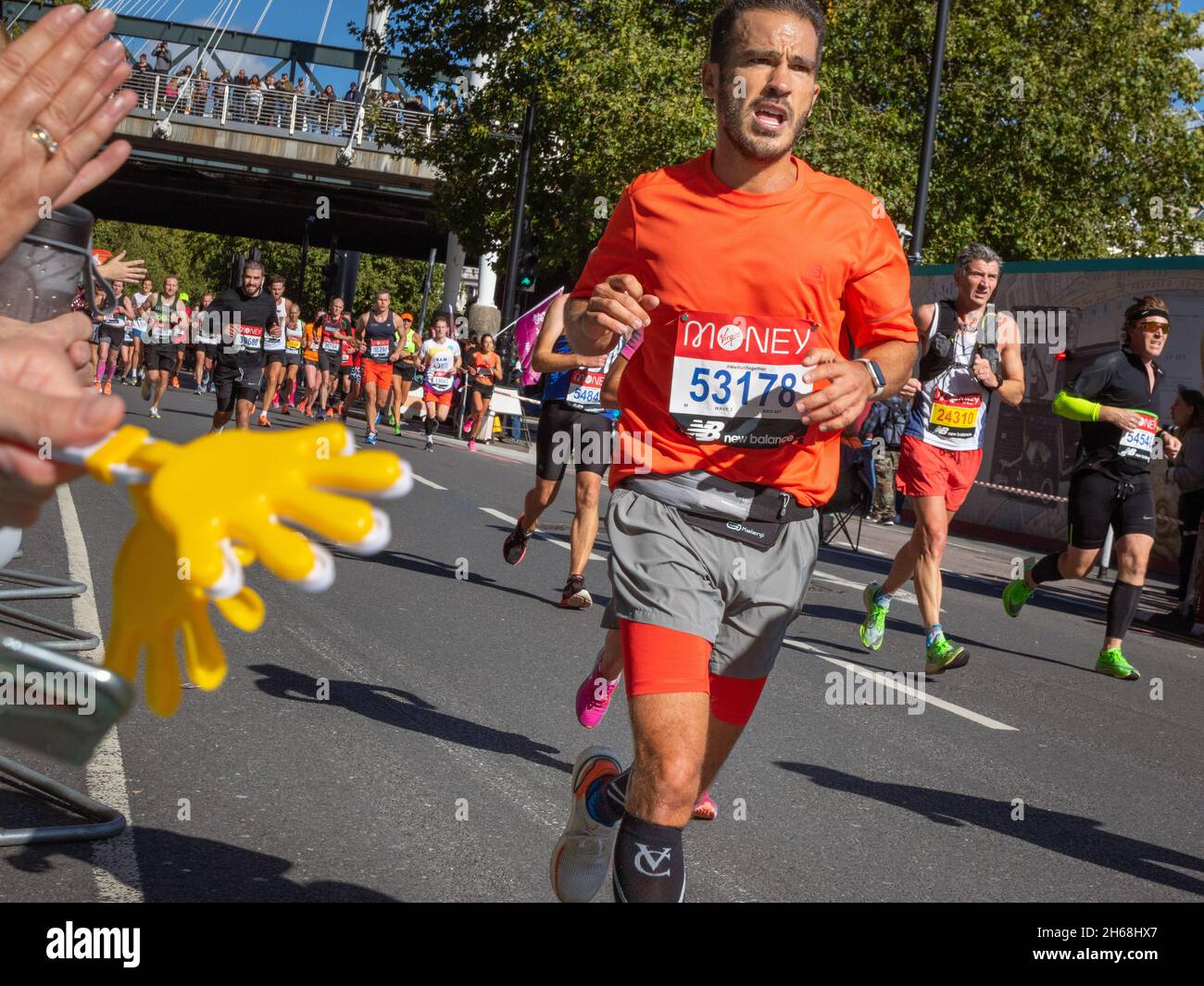 Man running with hand clappers waved in foreground, Virgin Money London Marathon 2021 at the 25 mile point, Victoria Embankment. Stock Photo