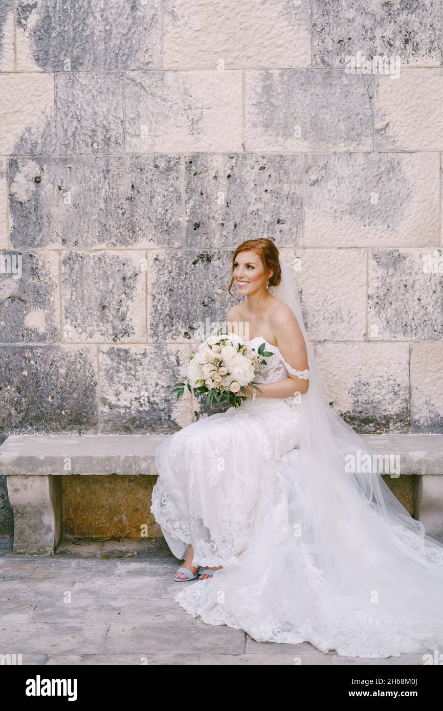 Bride in a white dress with a bouquet of flowers sits on a bench near a ...