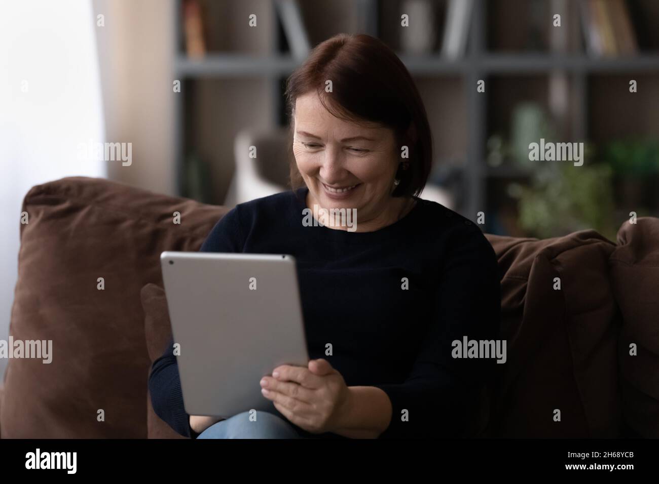 Close up smiling mature woman using tablet, sitting on couch Stock Photo