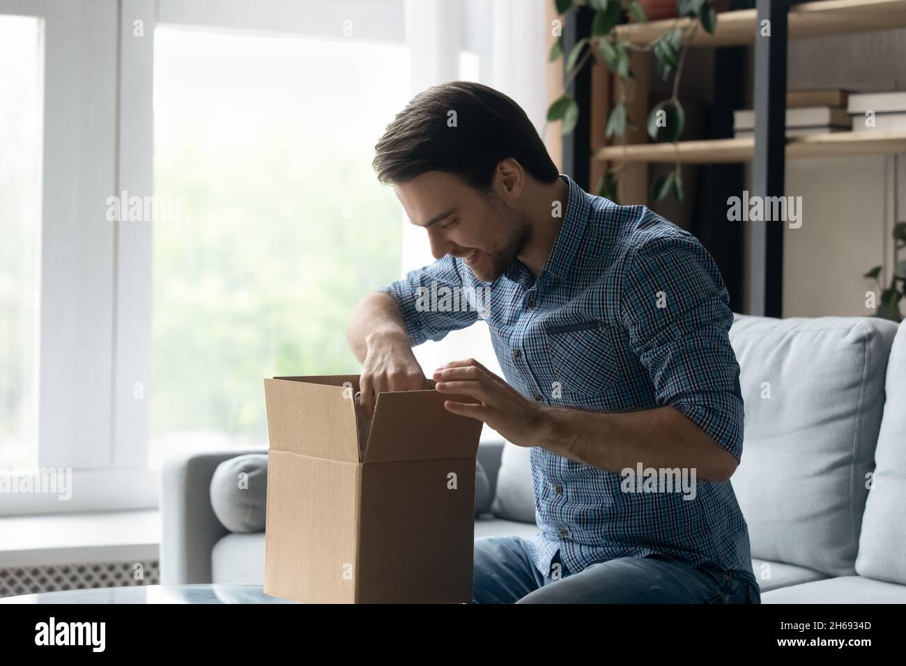 Happy young handsome man opening big cardboard box. Stock Photo