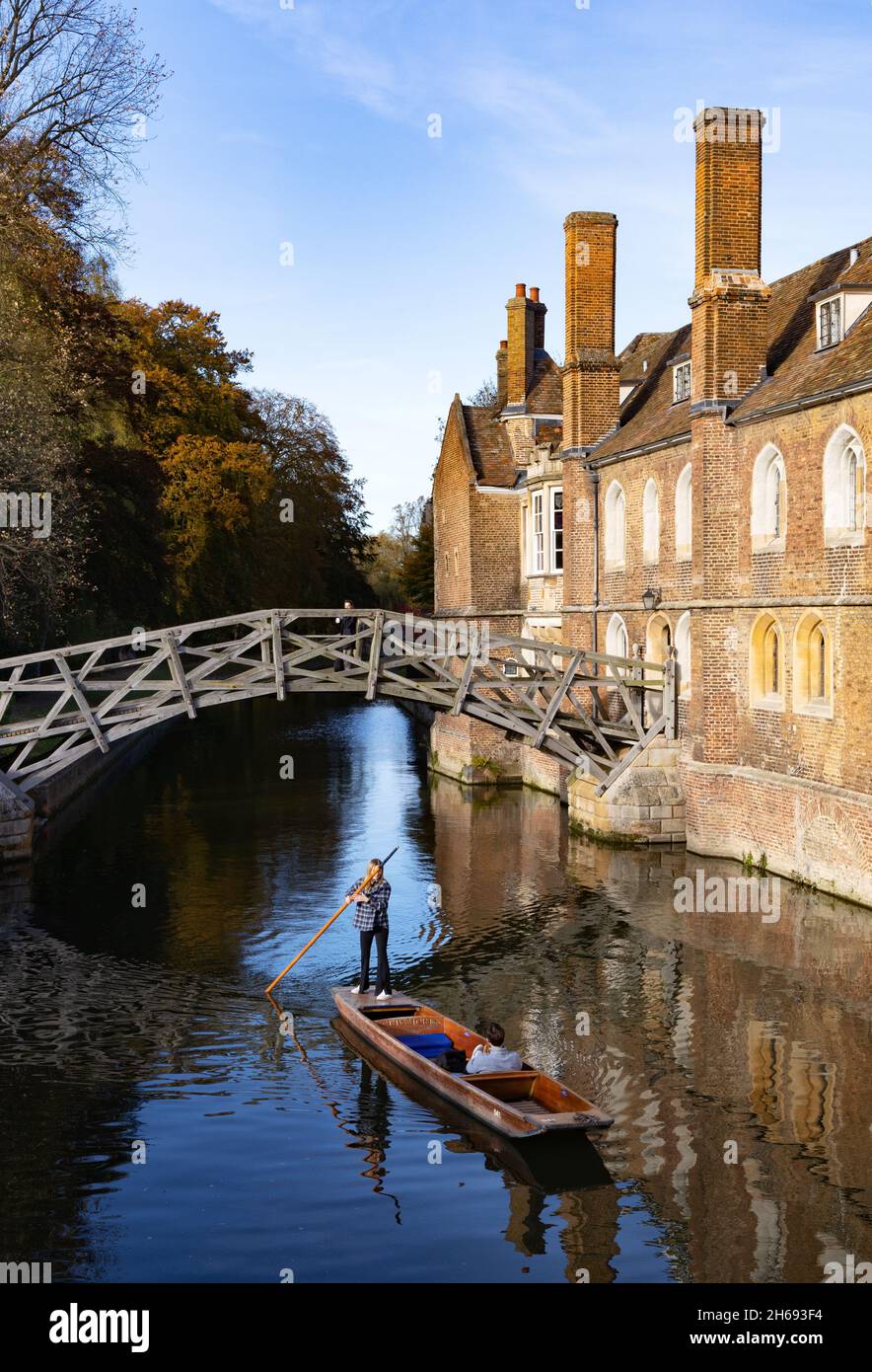 Punting Cambridge UK; a woman punting under Isaac Newton's Mathematical Bridge in autumn, Queens College Cambridge University, Cambridge England Stock Photo