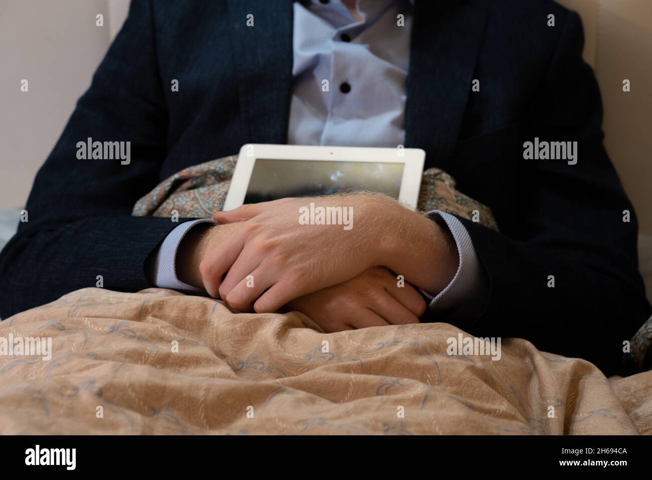 Covid-19 lockdown, work at home from bed. Man in suit with a laptop sits on bedroom  Stock Photo