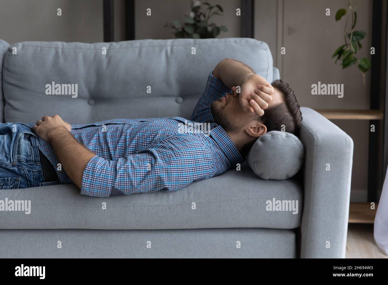Stressed young man sleeping on sofa at home. Stock Photo