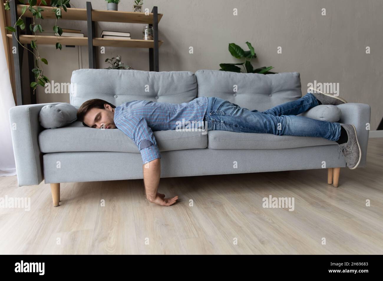 Exhausted young man fell asleep on comfortable couch. Stock Photo