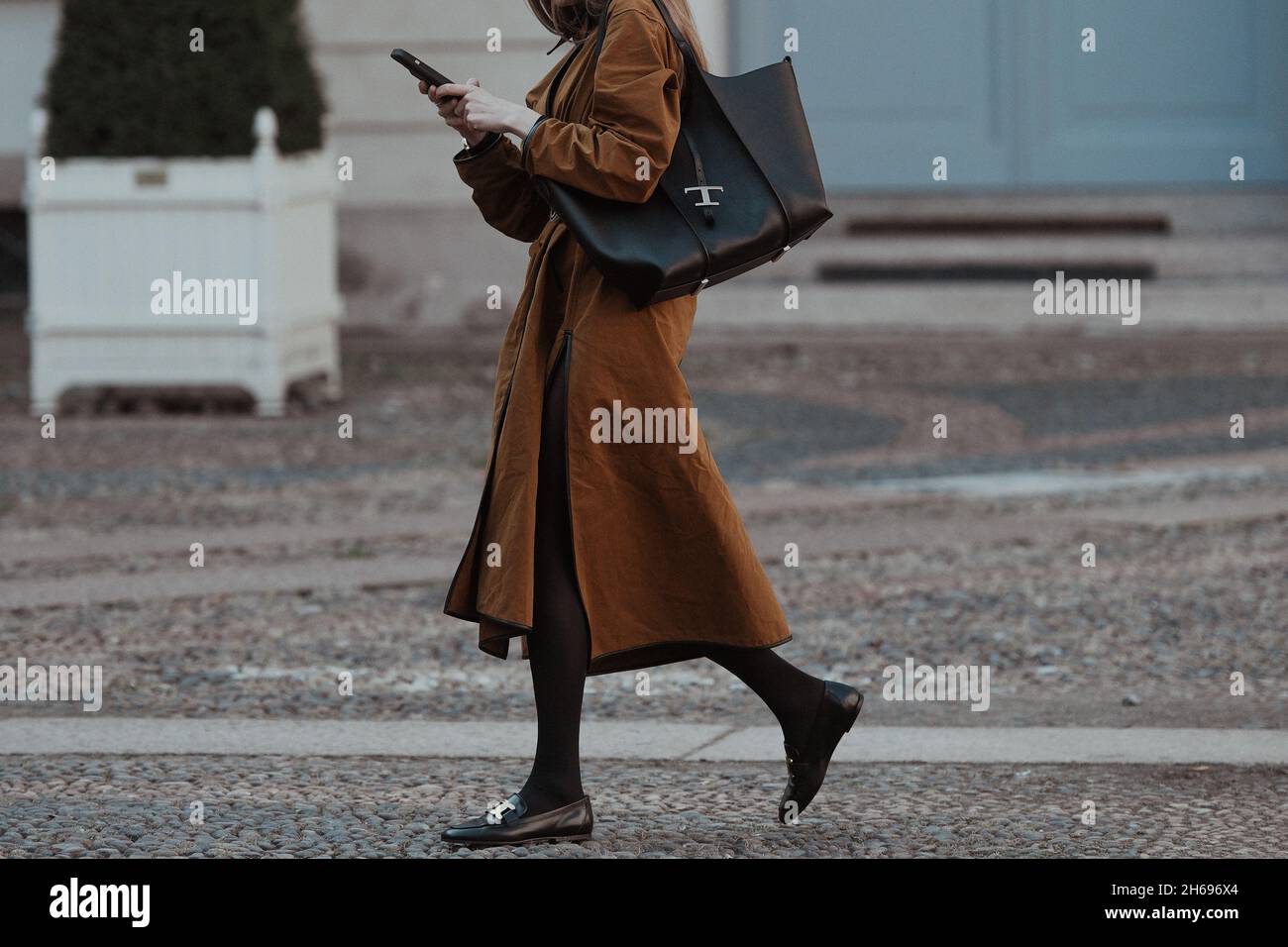 Milan, Italy - September 24, 2021:  Street style outfit, fashionable woman wearing a camel buttoned long oversized split coat, a black shiny leather b Stock Photo