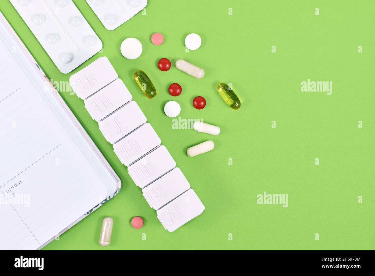 Pills, capsules, pill box and calendar on side of green background with