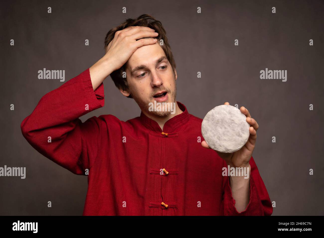 Young handsome tall slim white man with brown hair relieved holding pu erh tea cake in red shirt on grey background Stock Photo