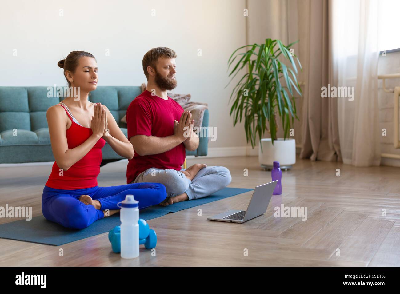 Middle aged couple meditating at home with online yoga tutorial. Stock Photo