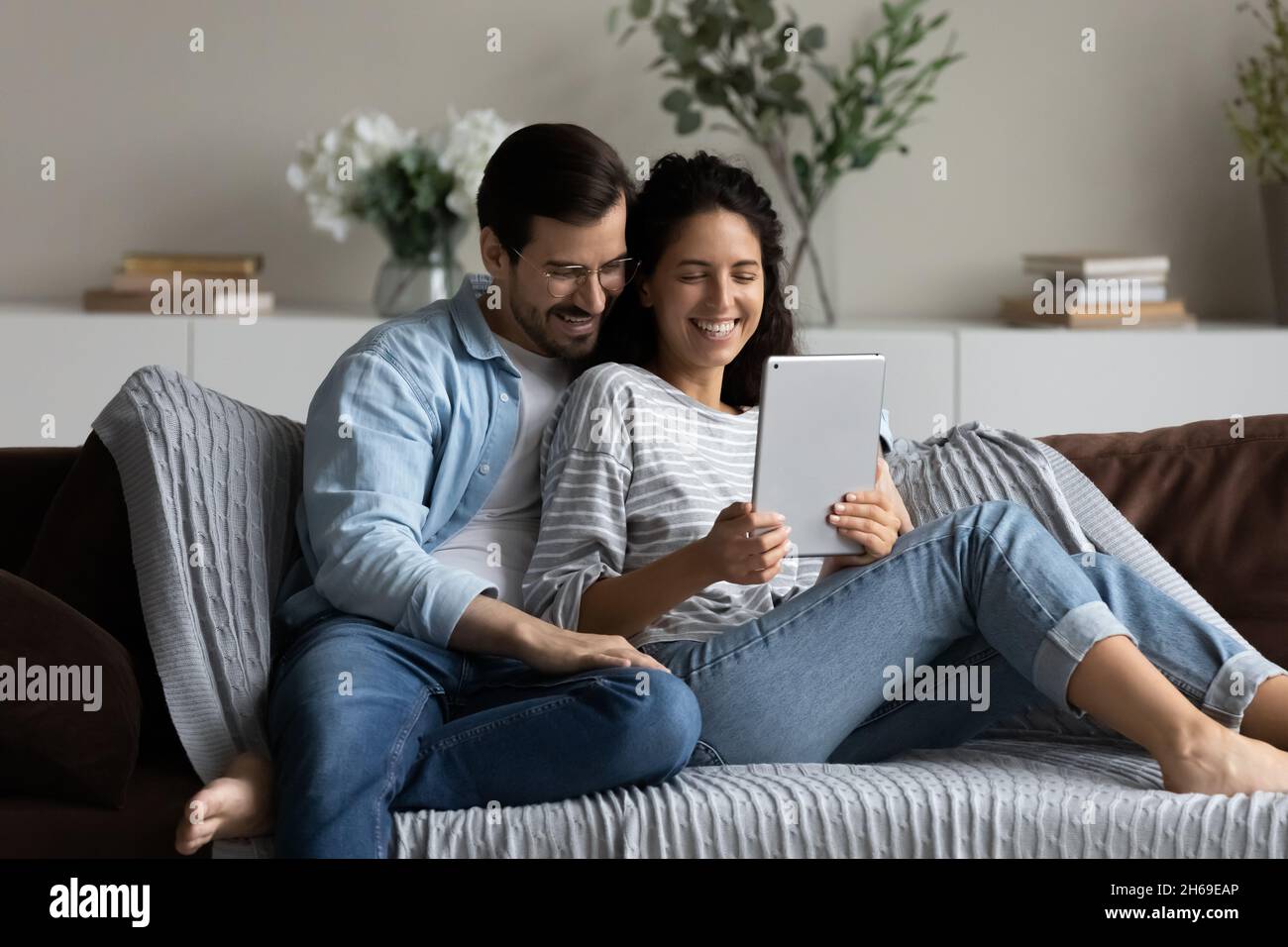 Happy couple hugging, using tablet together, relaxing on couch Stock Photo