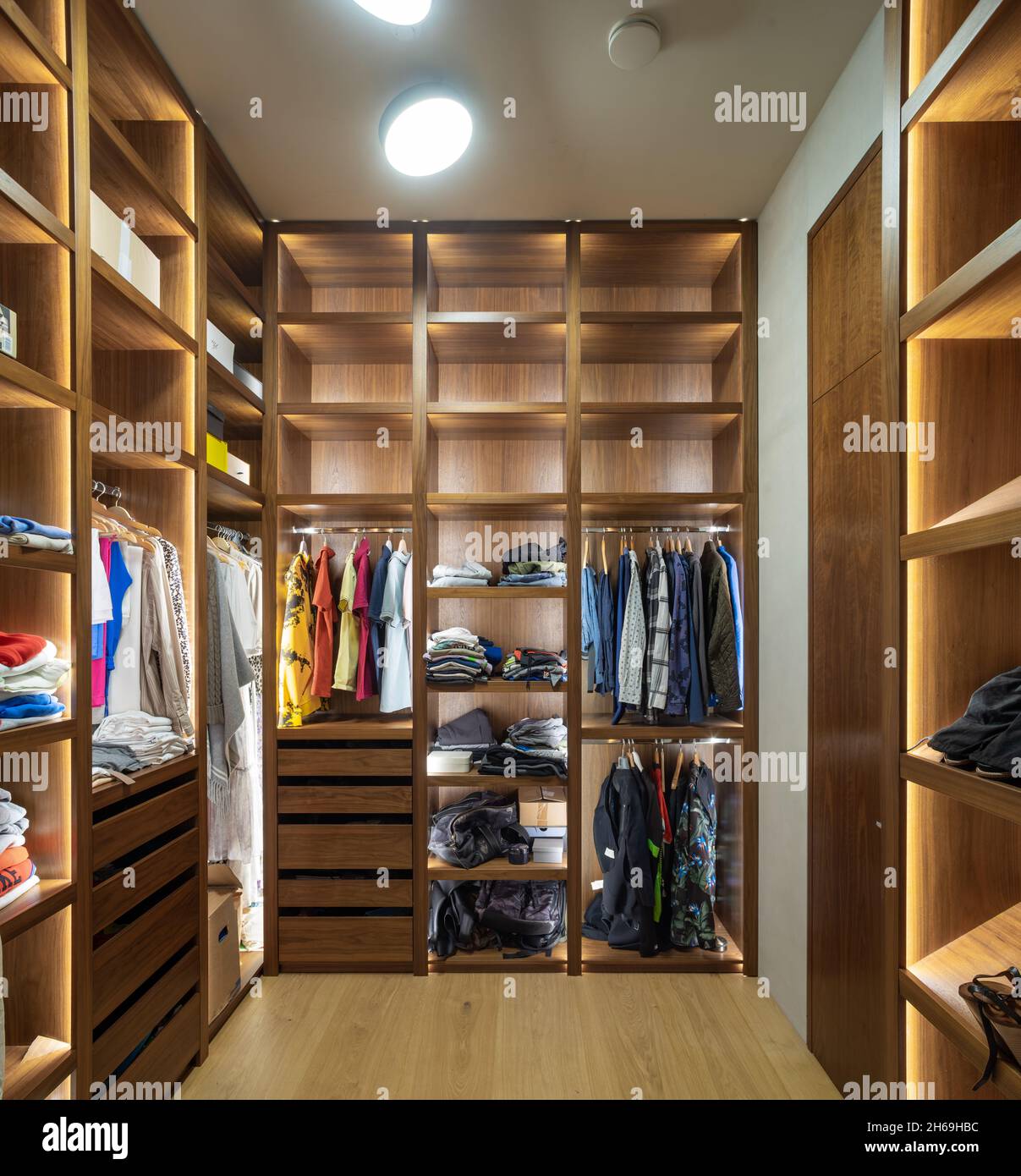 Modern interior of dressing room in luxury apartment. Illuminated wooden  shelves. Clothes on hangers Stock Photo - Alamy