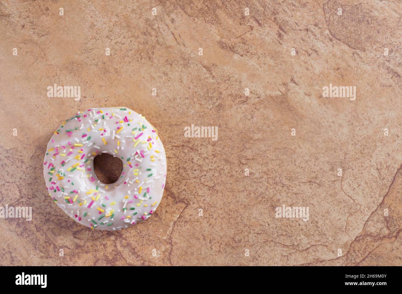 Glazed donut with colorful sprinkles on brown stone background, top ...