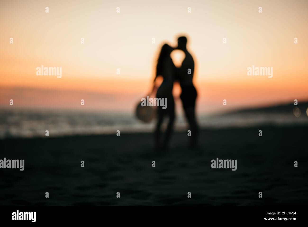A blurred shot of a romantic couple kissing silhouette on a beach with ...