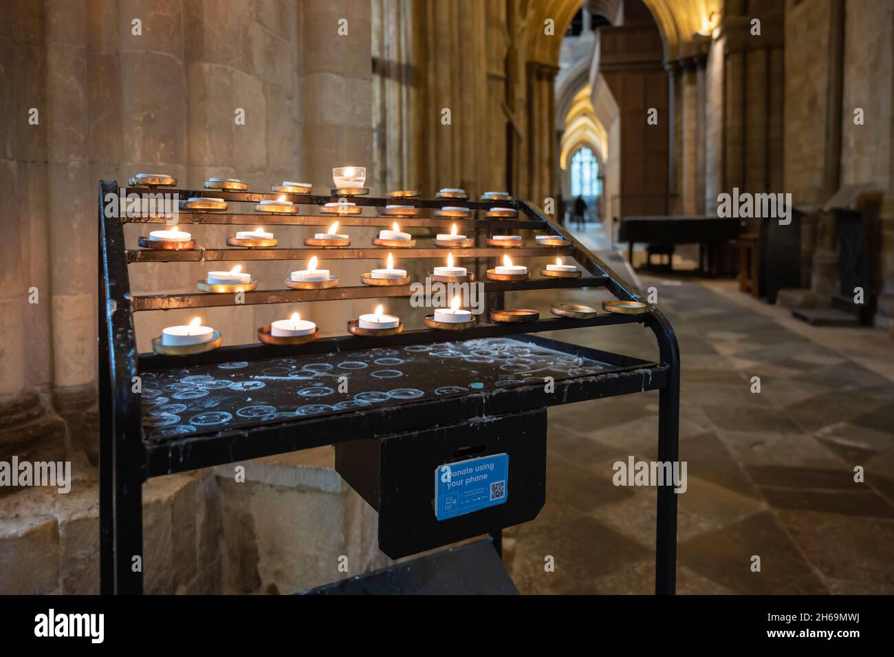 Votive or prayer candle rack with offering box in Chichester Cathedral in Chichester, UK. With thanks to The Dean & Chapter of Chichester Cathedral. Stock Photo