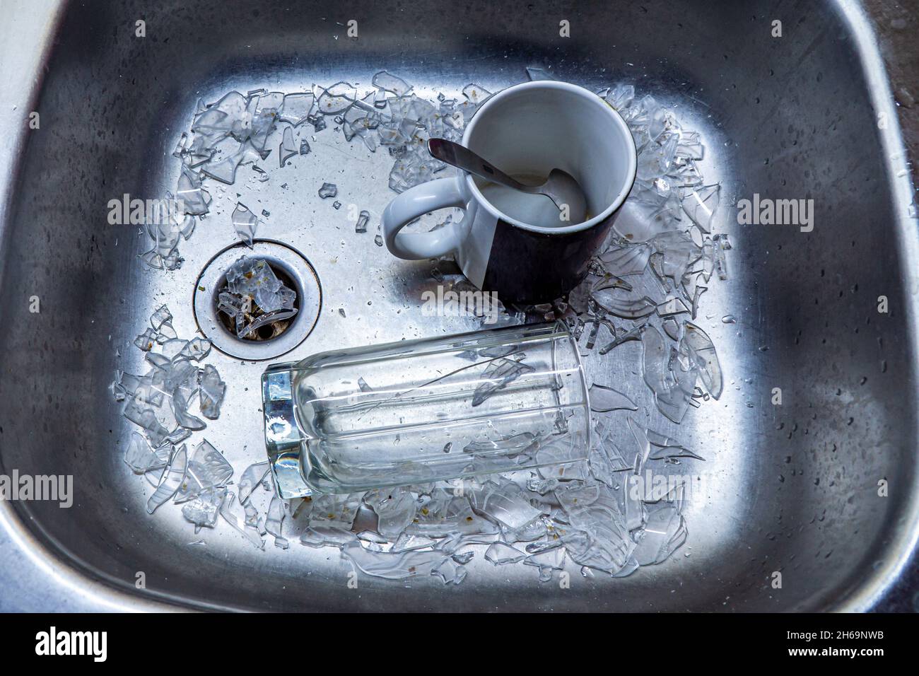 a broken glass in a pile of glass shards and a ceramic mug with a spoon