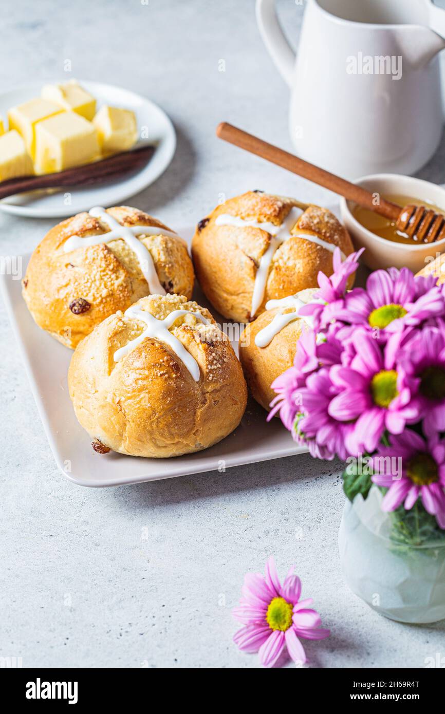 Traditional Easter cross buns with raisins, butter and honey on gray background with flowers. Stock Photo