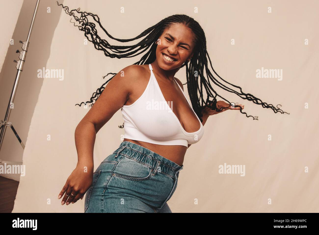 Cheerful young woman celebrating being natural in a studio. Happy young woman smiling and dancing while wearing denim jeans and a bra in a studio. You Stock Photo