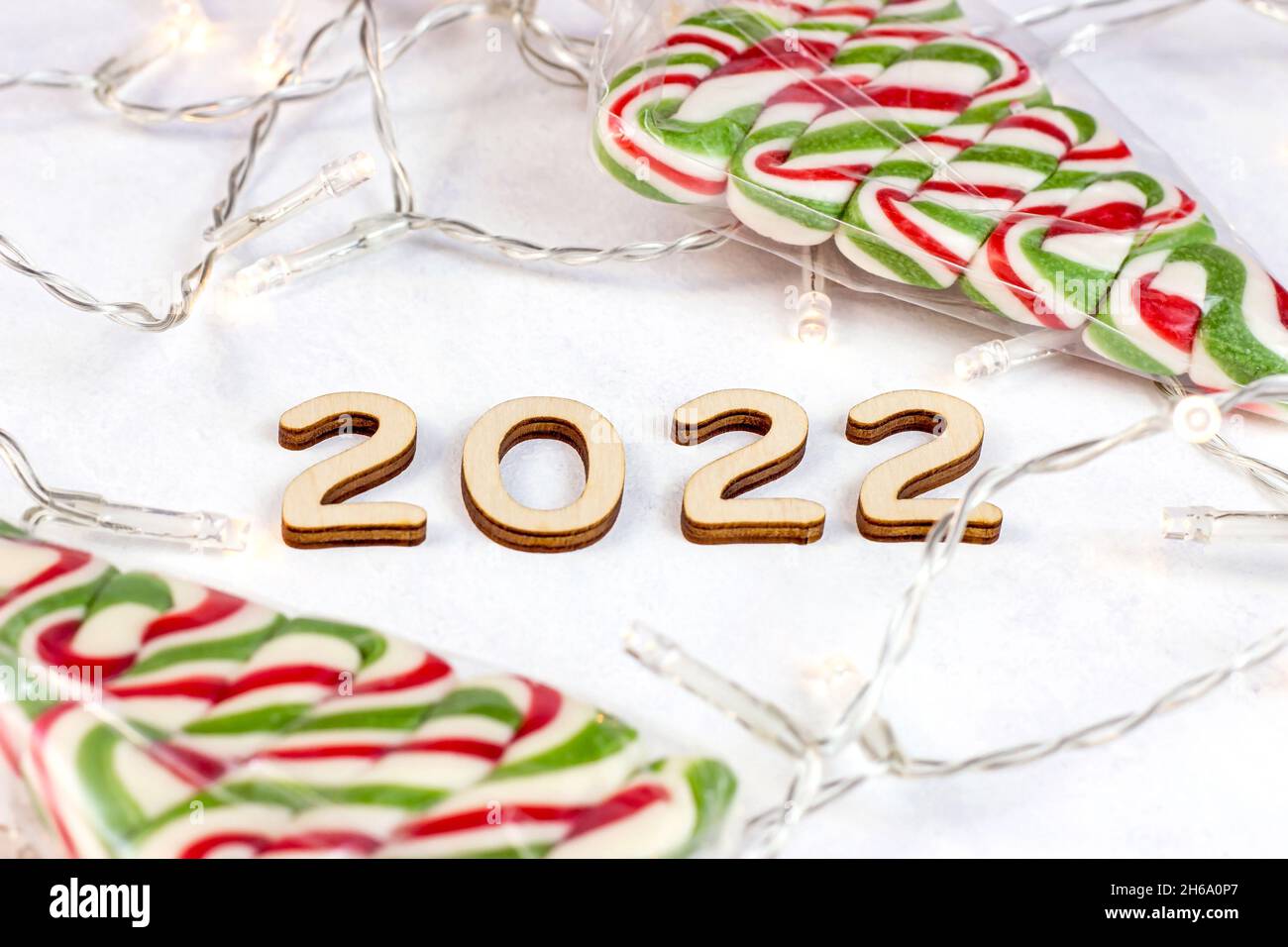 Wooden numbers 2022 silhouette with Christmas lights and sweet candies on light background. New Year beginning congratulations and planning concept. Stock Photo
