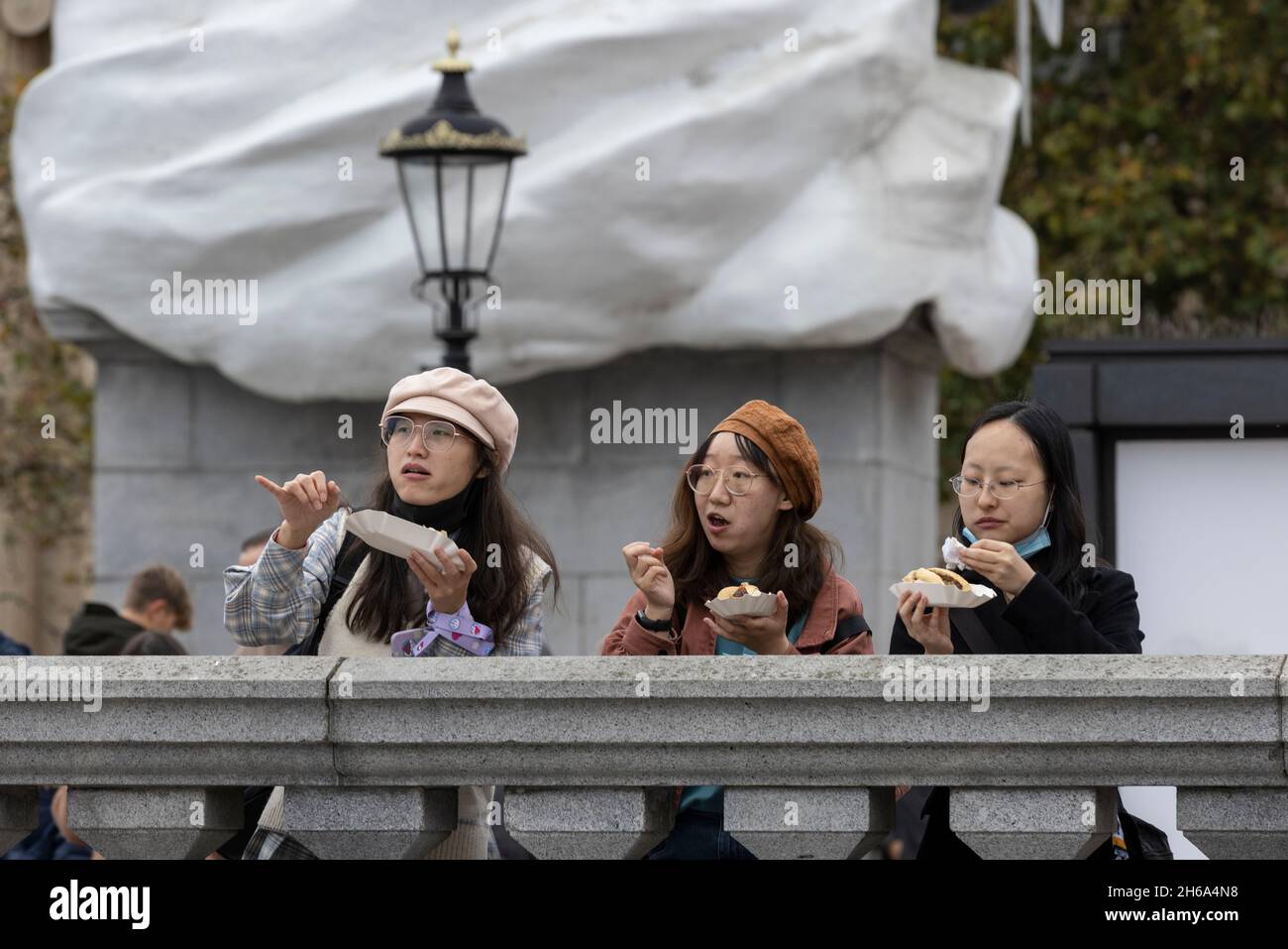 Chinese tourists eating takeaway lunch whilst standing in Trafalgar