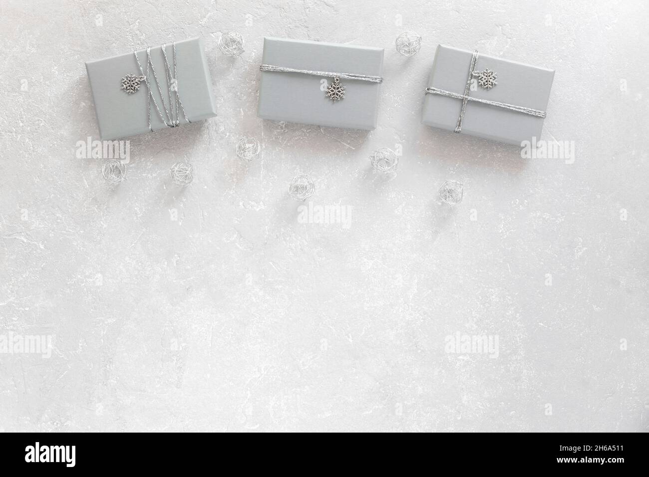 three grey gift boxes decorated with silver ribbon and snowflake pendant, on grey background, top view, copy space Stock Photo