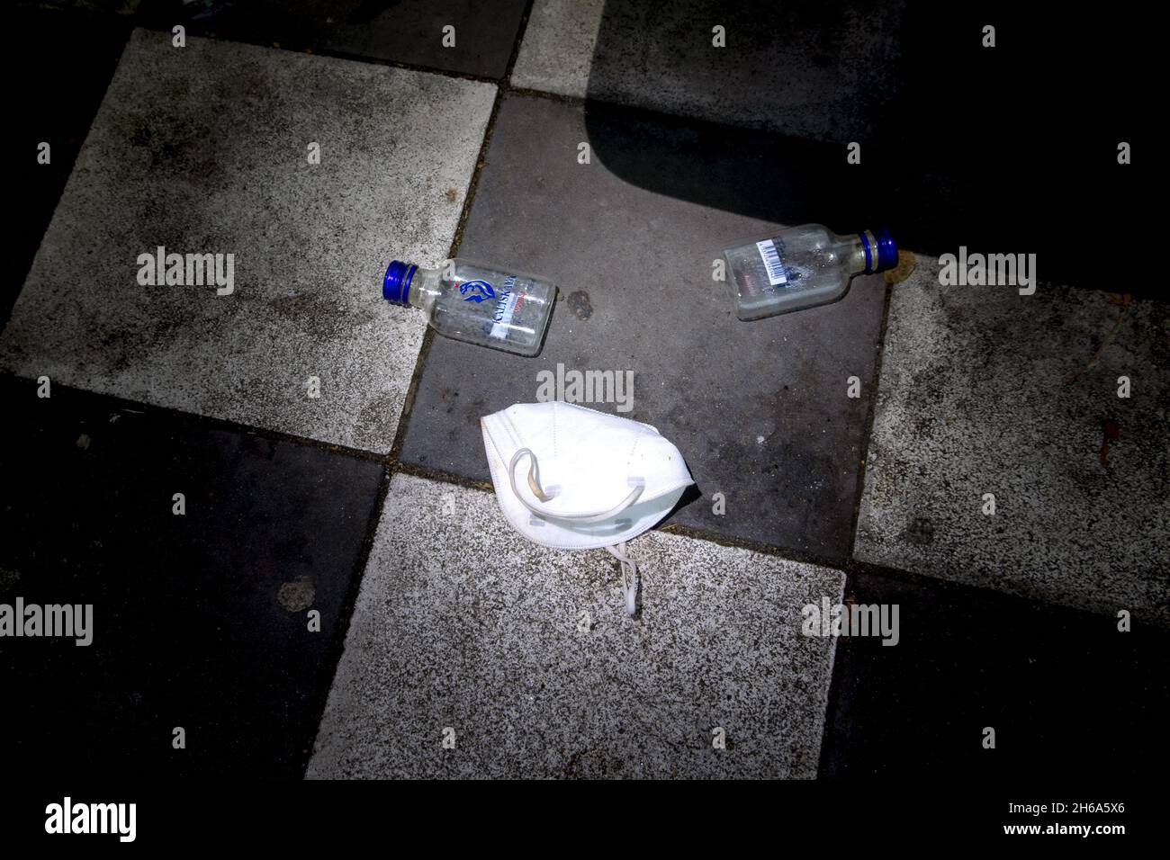 Zwei Wodkaflaschen auf dem Boden einer Bushaltestelle und eine weggeworfene FFP2 Maske. Stock Photo