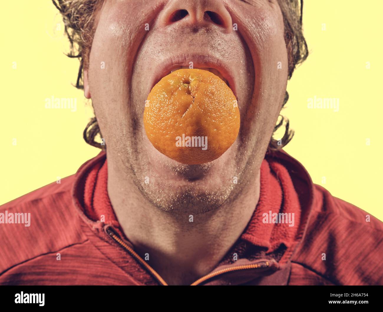 Man with big orange in mouth Stock Photo