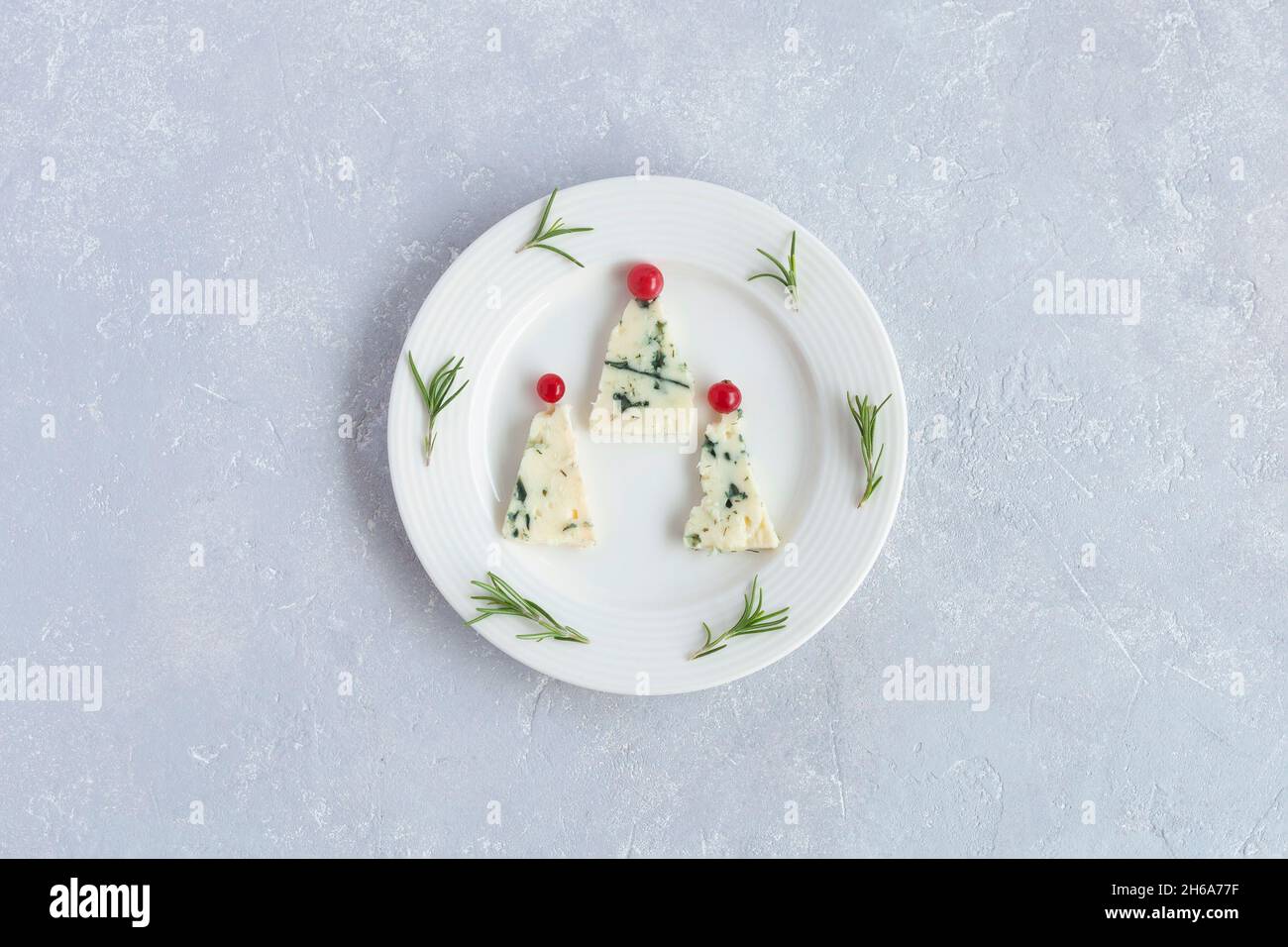 new year trees made of roquefort cheese and decorated with red currants, on a plate, grey background, top view Stock Photo