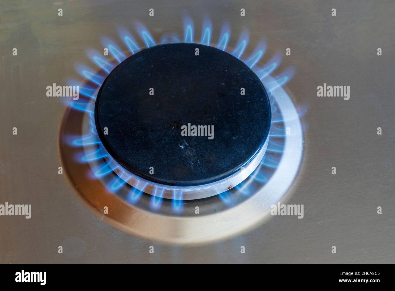 Gas ring alight on gas cooker hob. Circular grey ring topped with cast